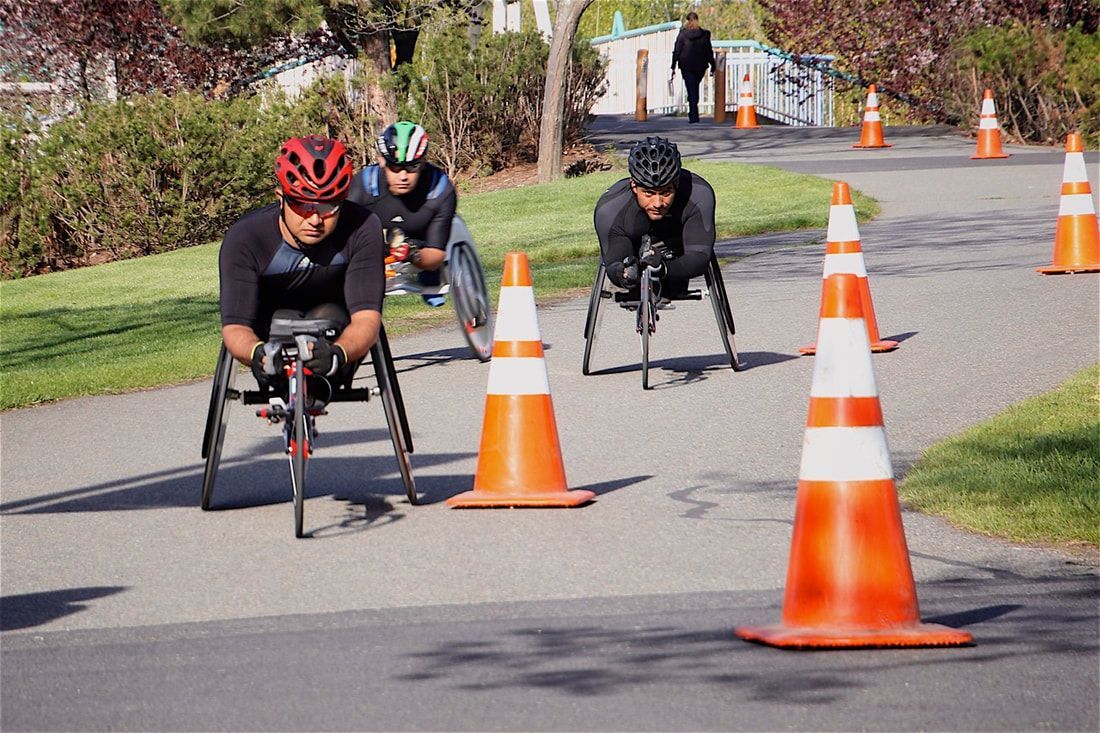 Three racers in dark shirts weave through orange cones on a park path