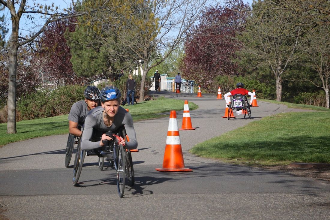 Two racers in gray shirts round a coned bend with another racer behind them