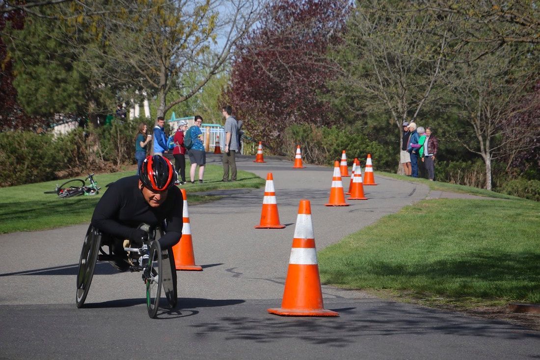 Racer in black with a red helmet takes a coned turn as spectators watch
