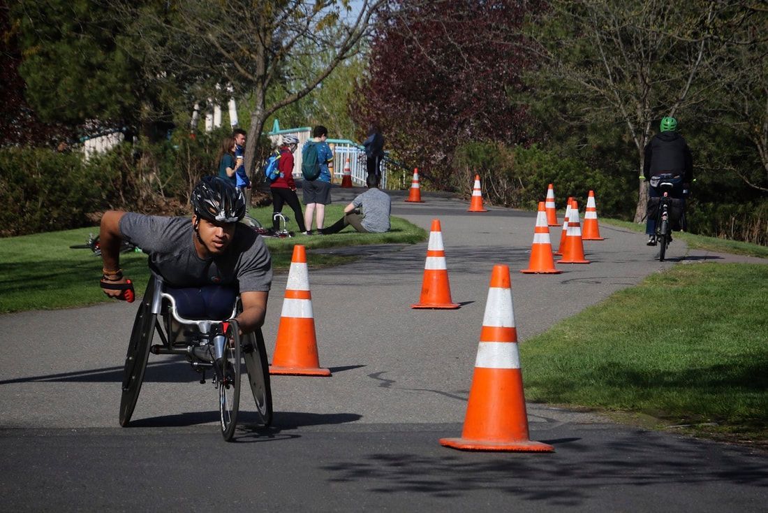 Racer in a gray shirt and black helmet swings an arm back on a coned course