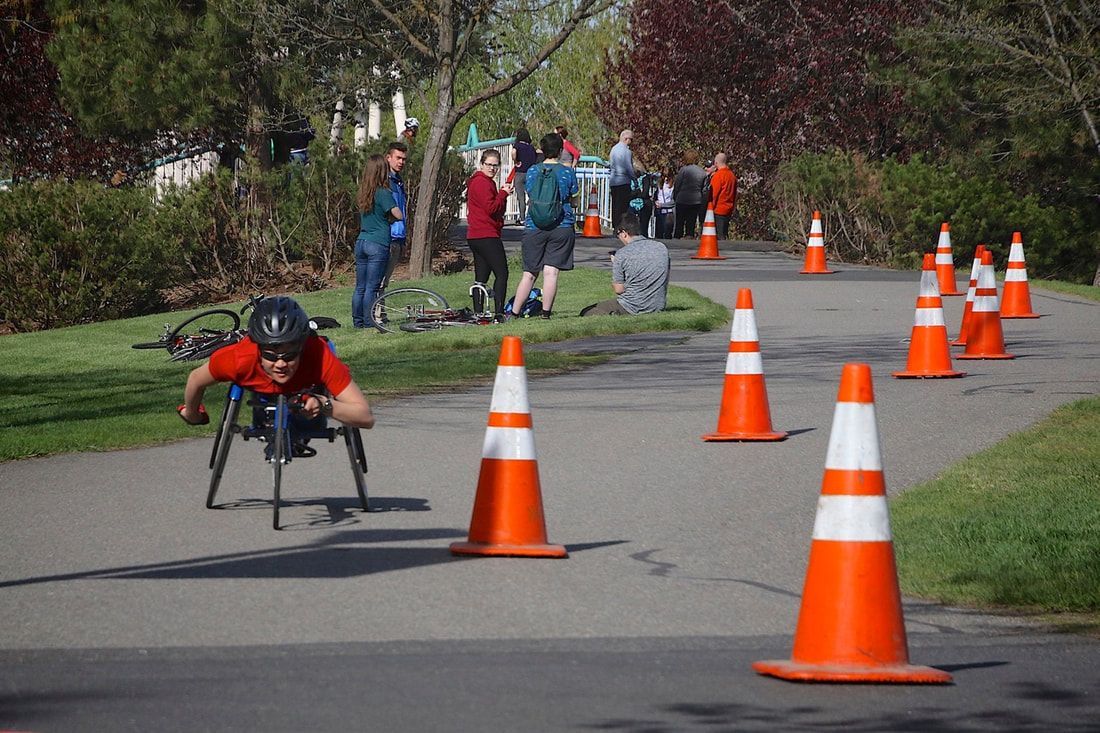 Racer in a red shirt tucks low behind a cone with spectators on the grass
