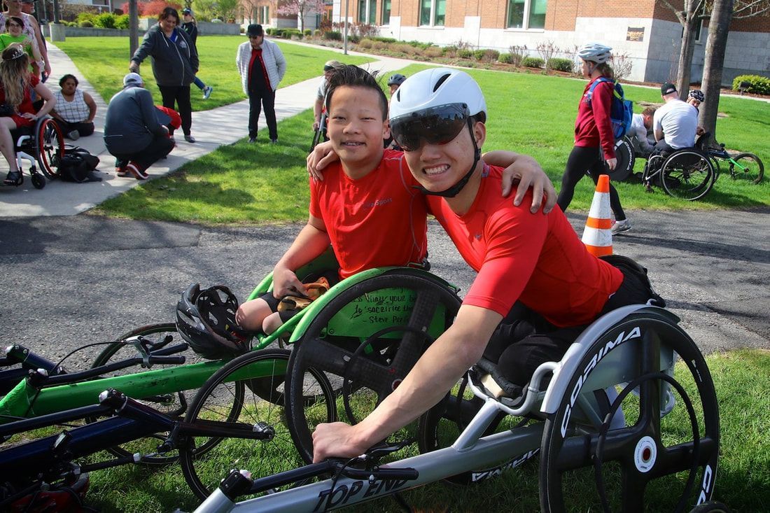 Two athletes in red shirts lean together in racing chairs on a lawn