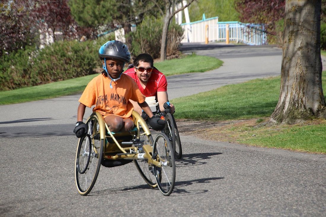 Young racer in an orange shirt in a gold chair with a man in red close behind