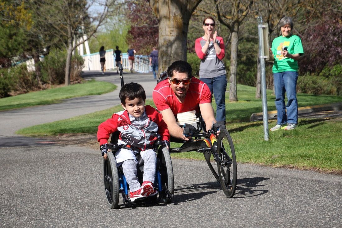 Man in a racing chair rolls beside a smiling boy in a wheelchair as fans clap