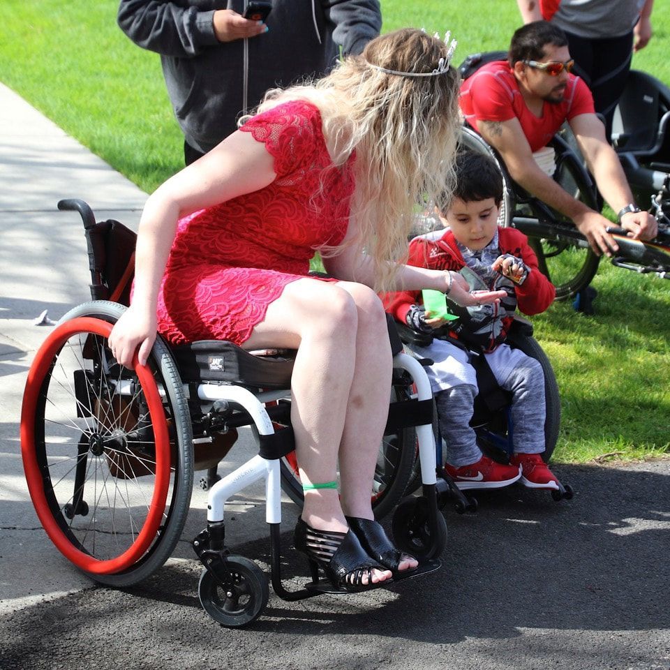 Woman in a red dress in a wheelchair leans toward a boy in a wheelchair