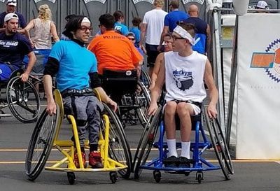 Young player in a #Elite jersey sits beside a player in a yellow wheelchair