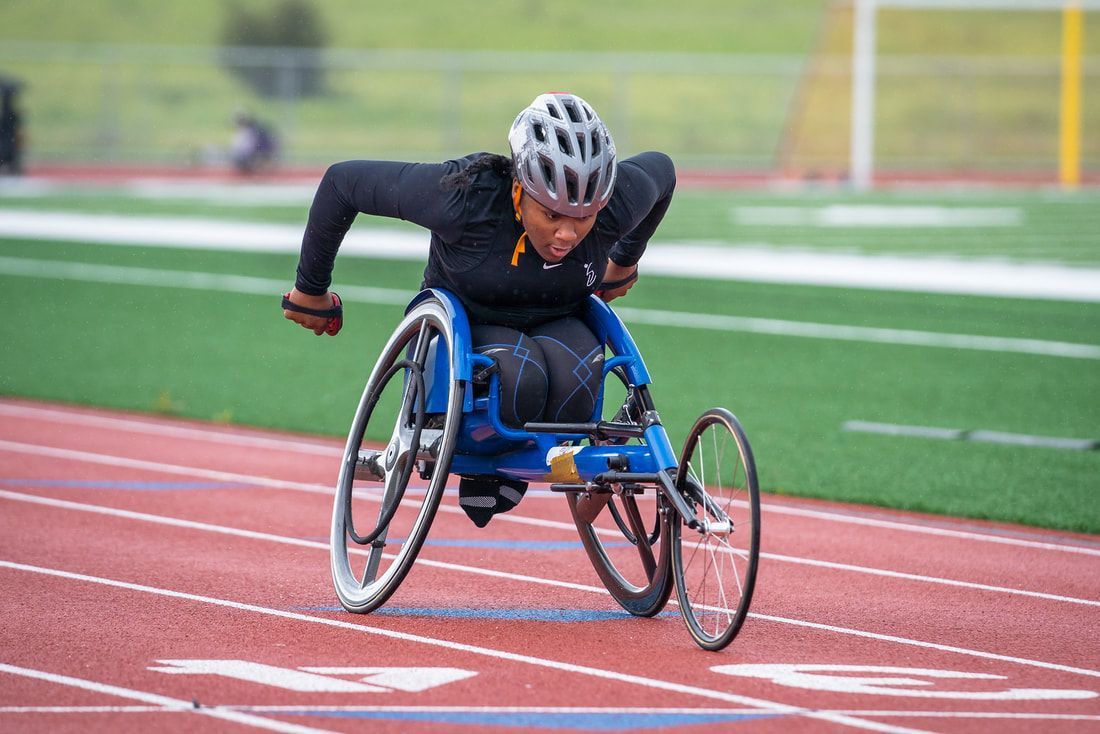 Athlete in a racing wheelchair and helmet speeds around the track