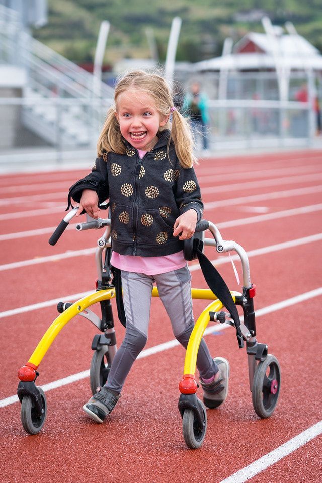 Smiling child walks down the track using a yellow walker