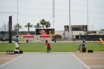 Young athlete in red throws a javelin from the runway as officials watch