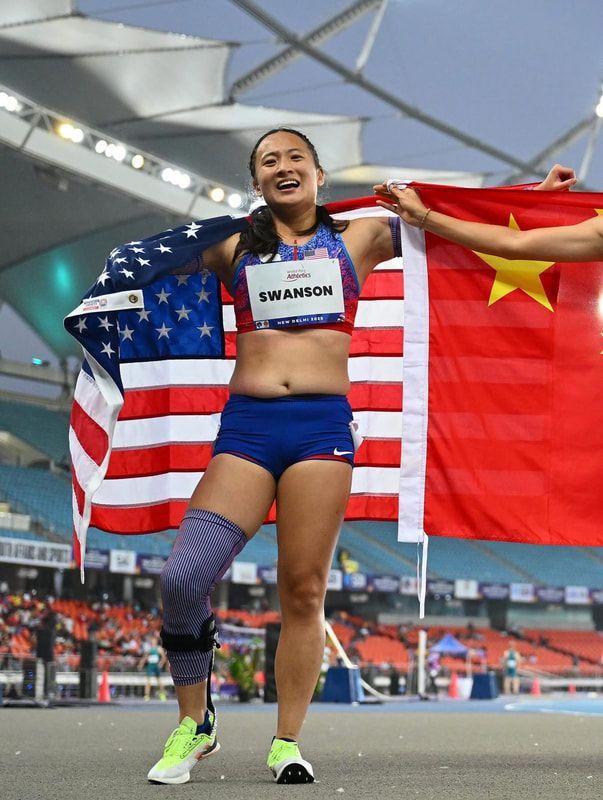 Smiling Team USA sprinter holds up an American flag on the track