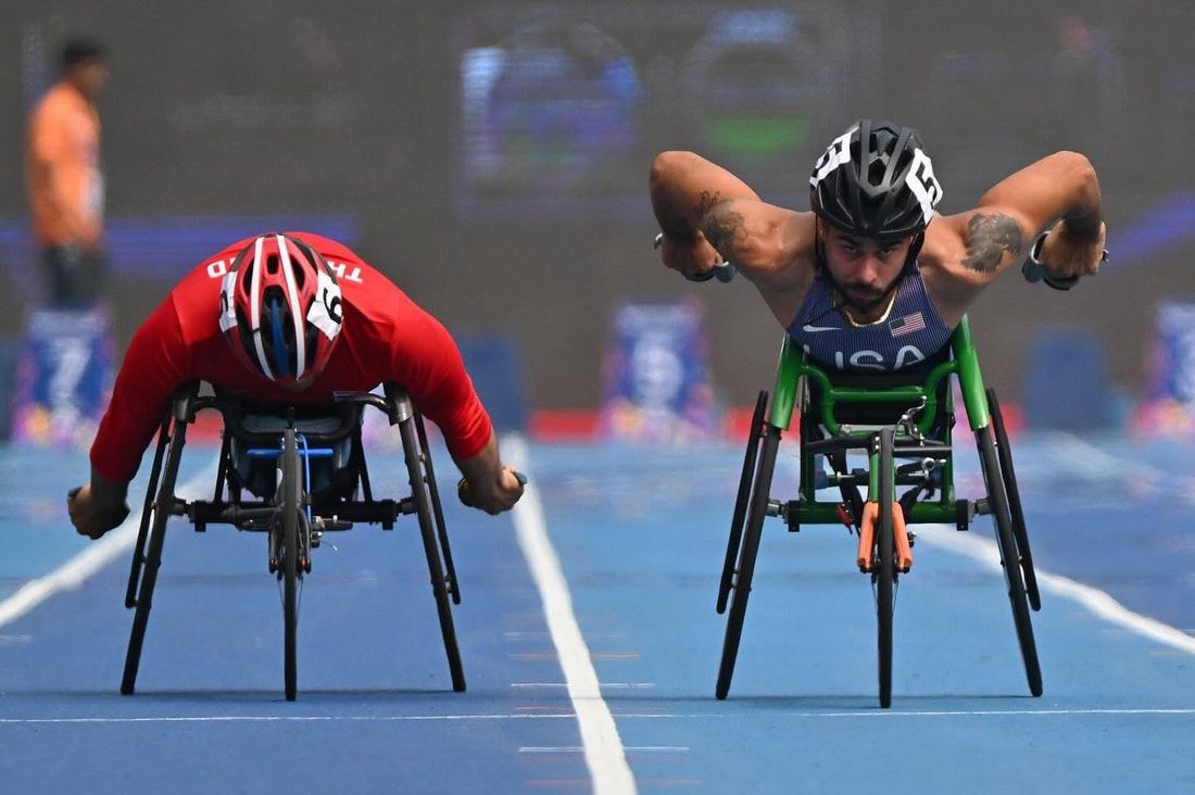 Two wheelchair racers, one in Team USA blue, lean low as they race