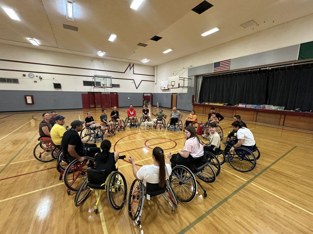 Group in basketball wheelchairs sits in a circle at center court