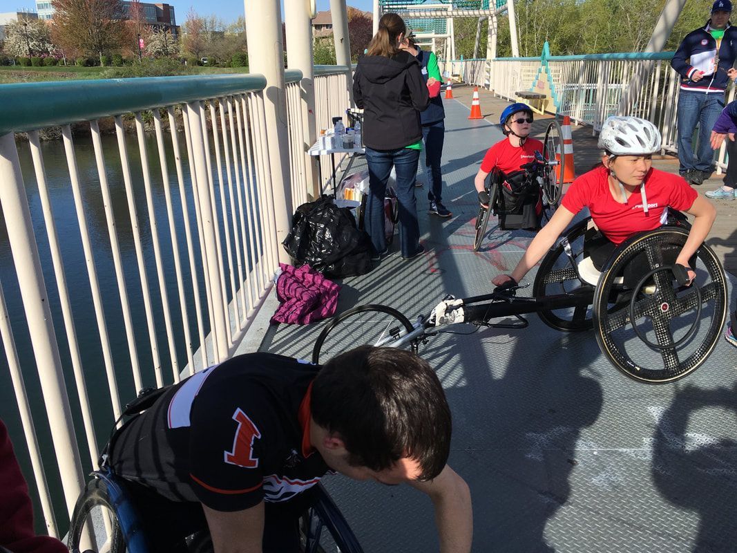 Racers in red shirts get ready on a footbridge beside a pile of bags