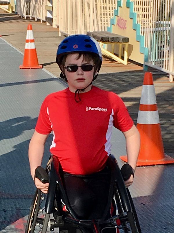 Young athlete in a blue helmet and red ParaSport shirt sits in a wheelchair