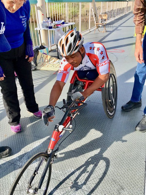 Racer in a stars-and-stripes jersey adjusts a red racing chair on a bridge
