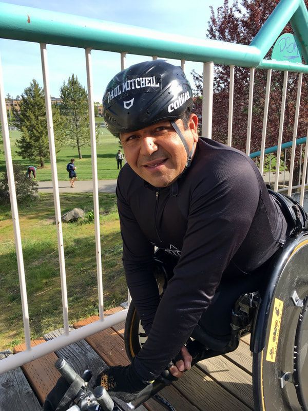 Smiling racer in a black helmet and long sleeves poses on a footbridge