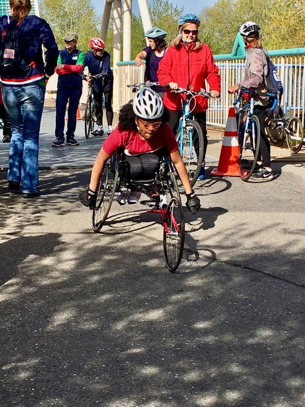 Young racer in a white helmet heads out as cyclists and volunteers look on