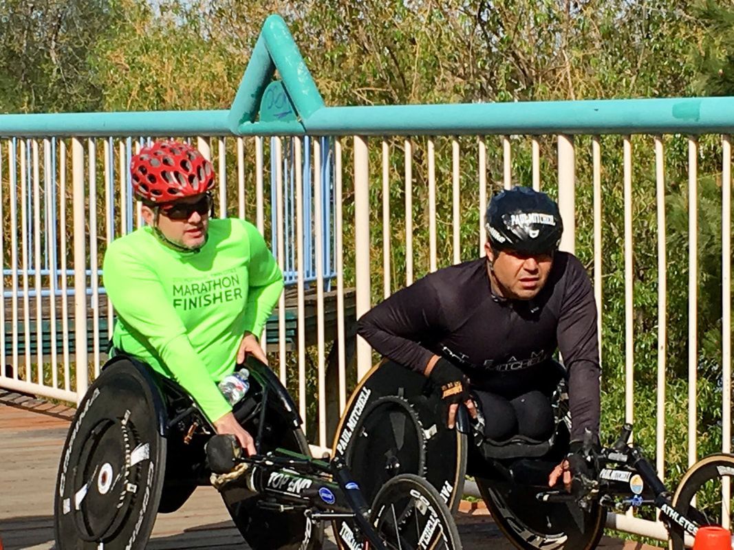 Two racers chat on a footbridge, one in a green Marathon Finisher shirt