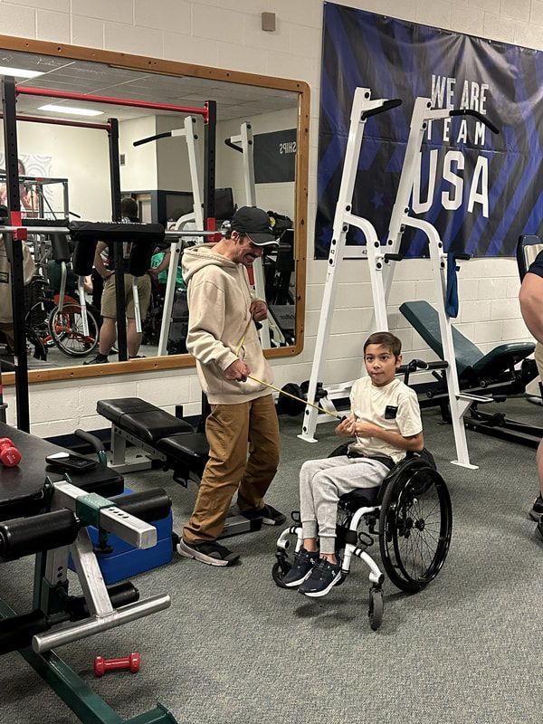 Coach works with a young athlete in a wheelchair in the weight room