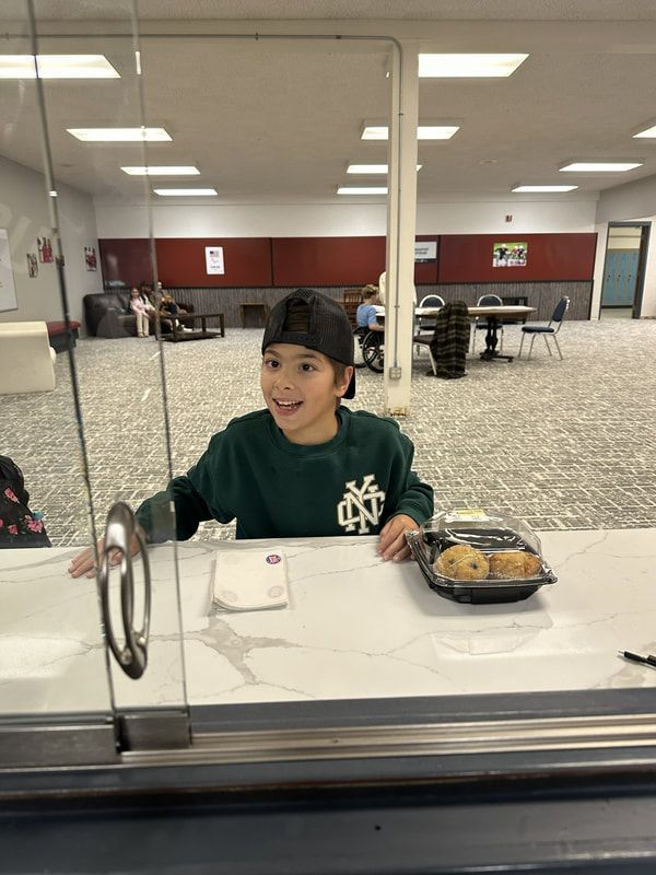 Smiling child in a green sweatshirt at the front window counter with cookies