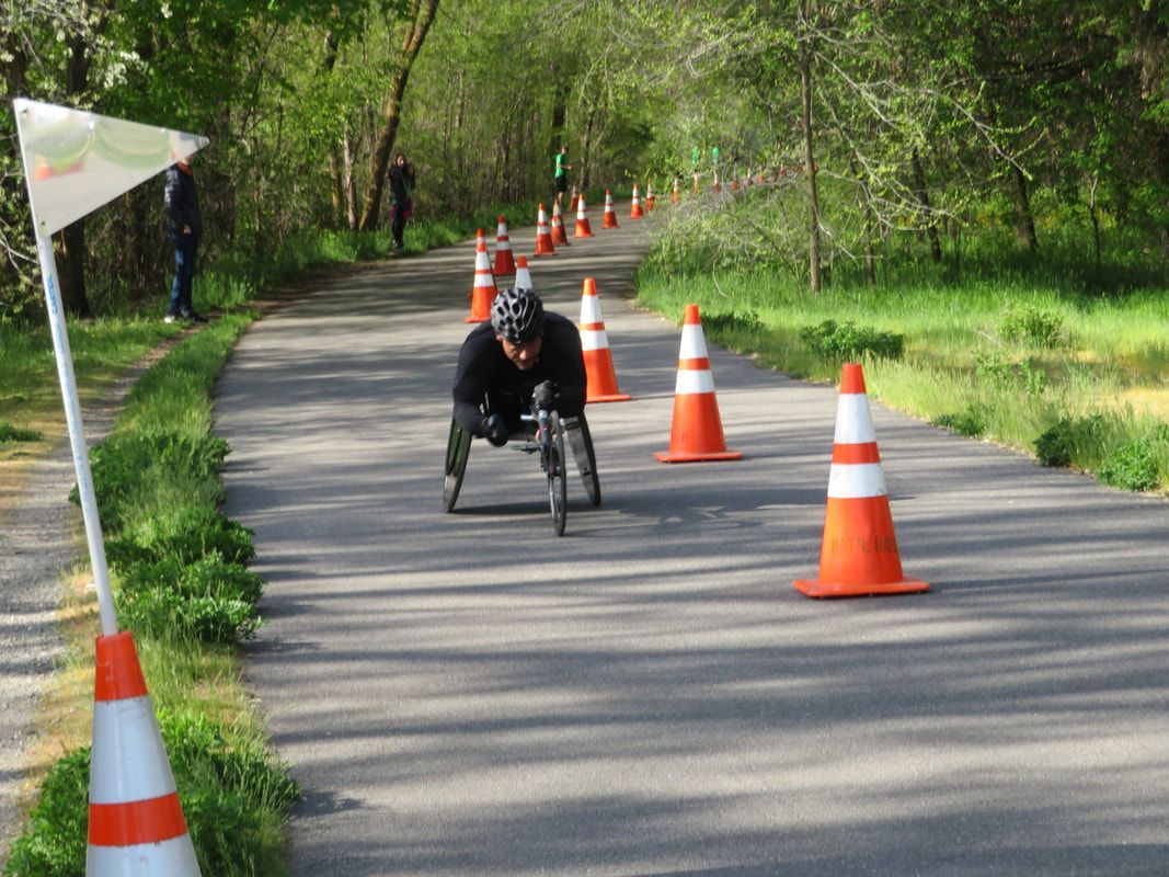 Racer in black heads down a tree-lined trail marked with cones and a flag