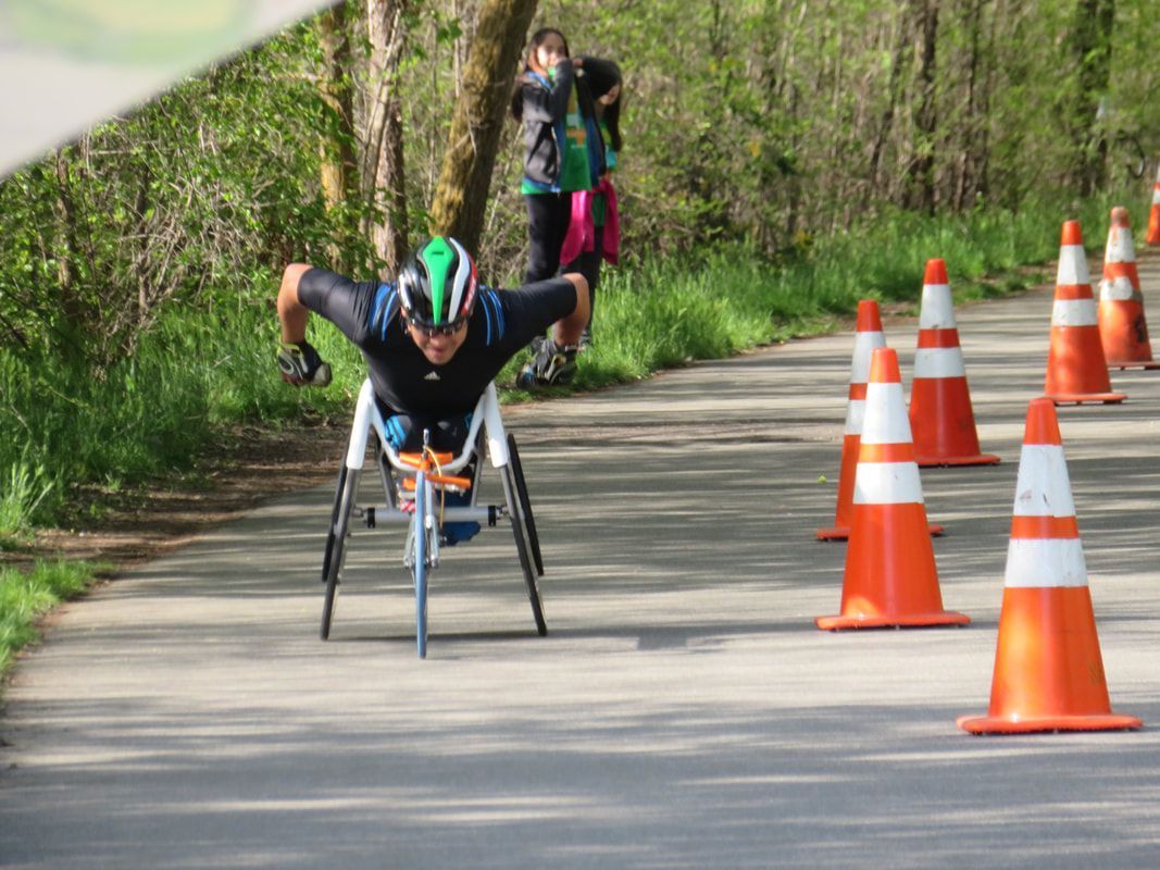 Racer in a green and white helmet with arms spread rolls down a coned path