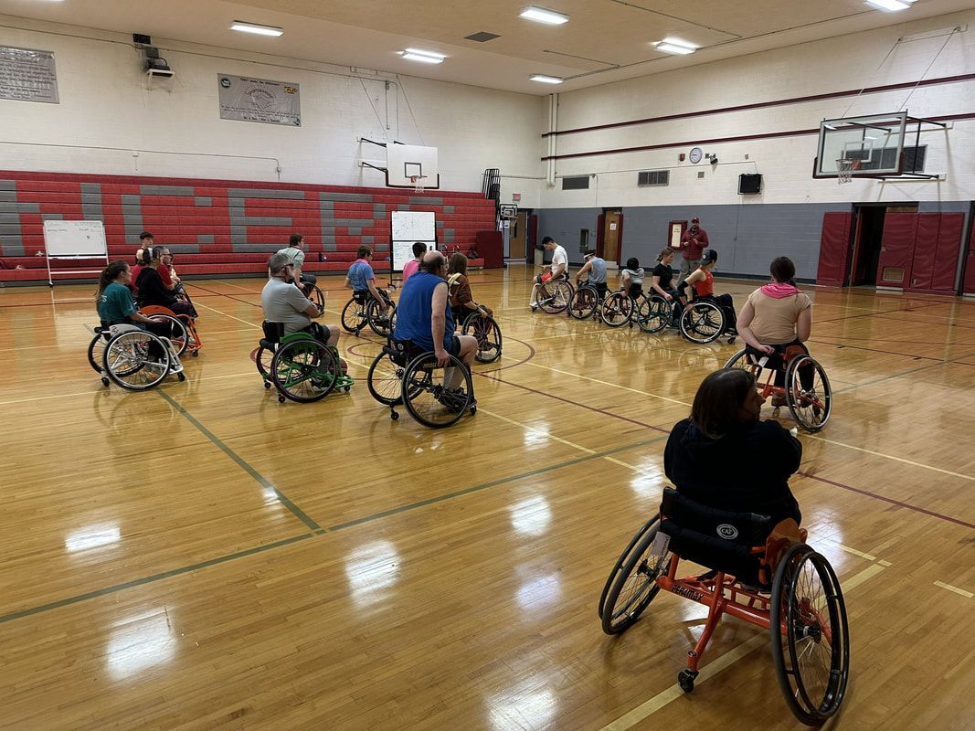 Athletes in basketball wheelchairs spread out on the gym floor for drills