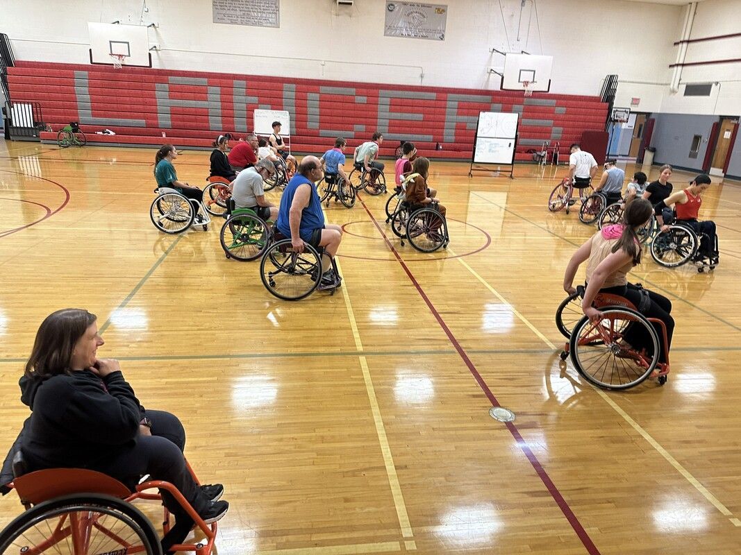 Wheelchair basketball practice in the gym in front of red Lancers bleachers