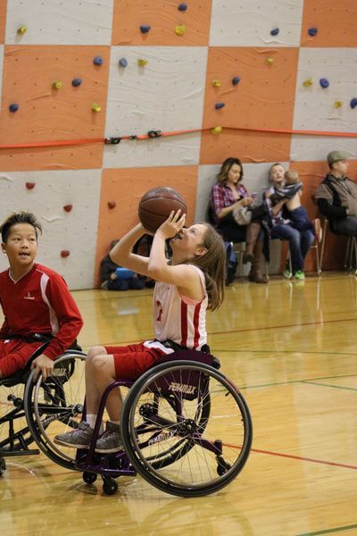Young player shoots from her wheelchair in front of a climbing wall