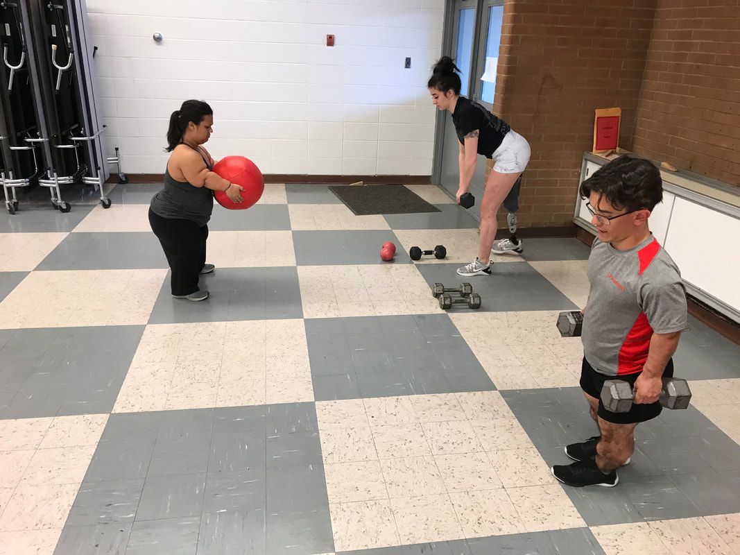 Athletes train with a medicine ball and dumbbells, one on a prosthetic leg