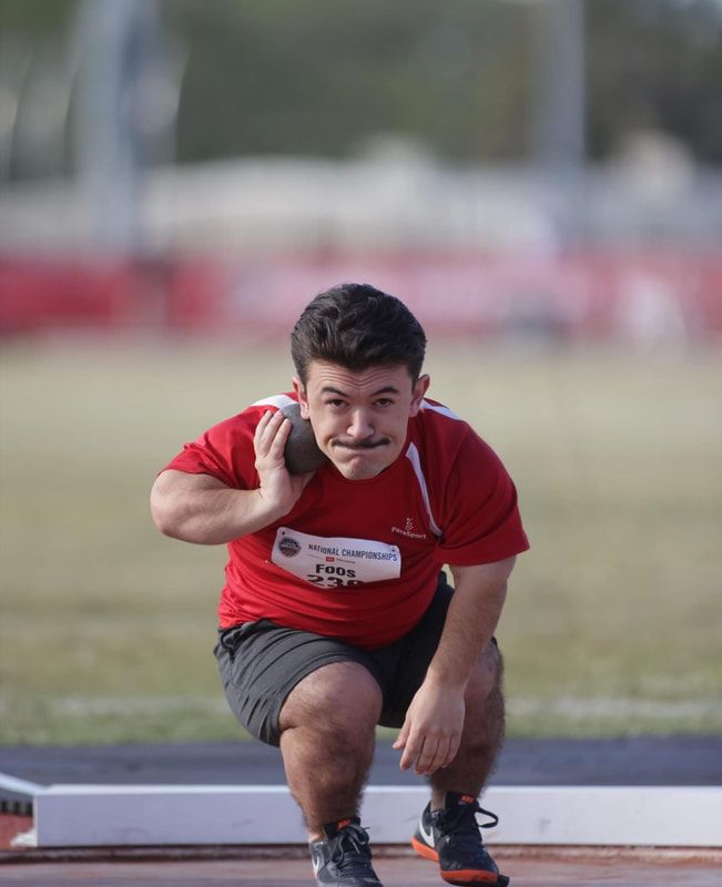 Shot putter in a red ParaSport shirt crouches low, ready to throw
