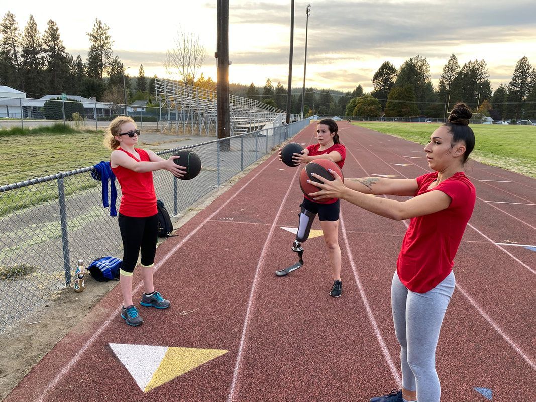 Three athletes in red pass medicine balls on an outdoor track