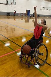 Player in red wearing a face mask practices shooting in her basketball chair