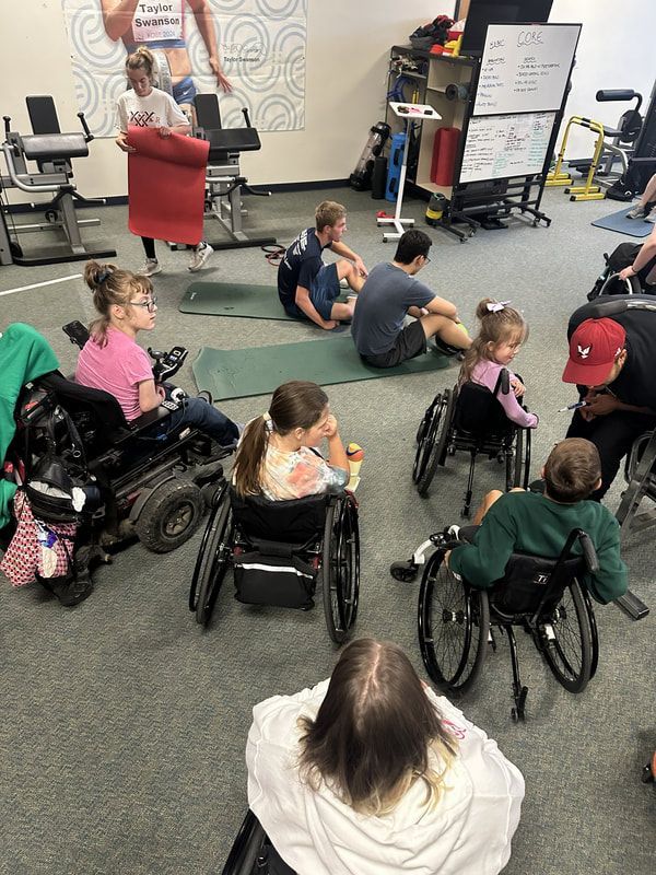 Young athletes, many in wheelchairs, watch a coach demo in the training room