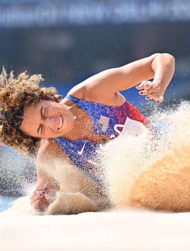 Team USA long jumper lands in a spray of sand, eyes squeezed shut