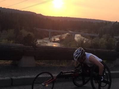 Racer in a racing wheelchair passes a river overlook at sunset