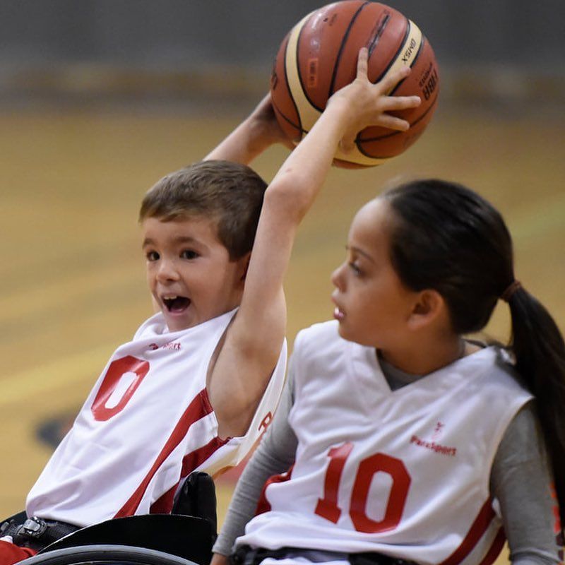 Young player in jersey 0 holds a ball overhead beside a teammate in 10