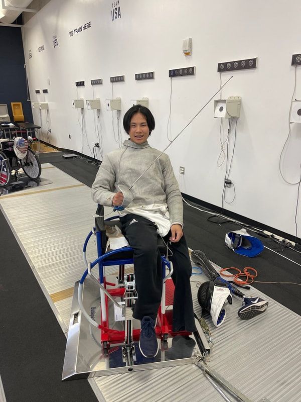 Jackson Atwood in fencing whites sits in a wheelchair fencing frame