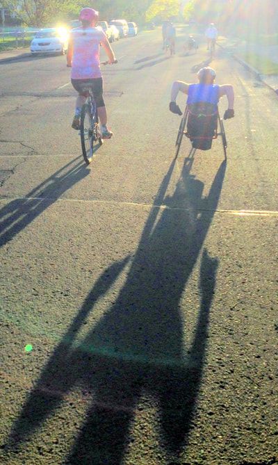 Cyclist and racer ride away into the sun, casting long shadows