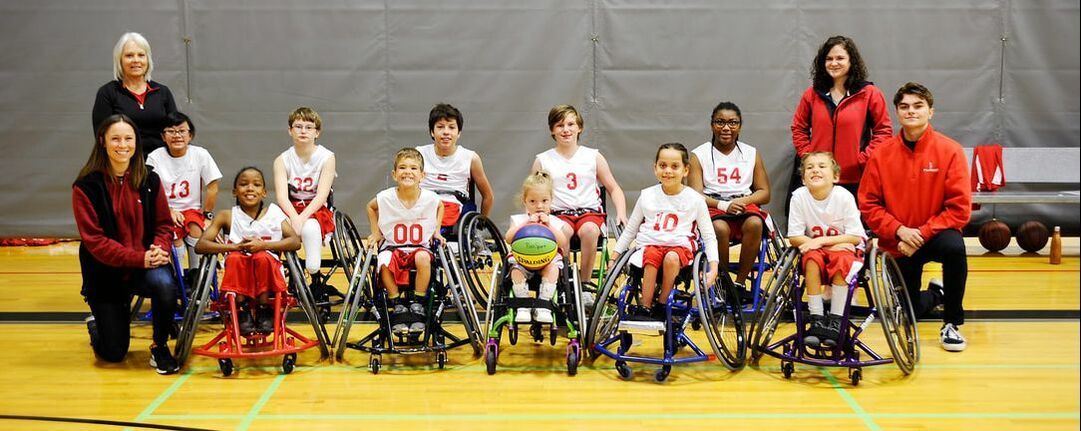 Youth wheelchair basketball team and coaches pose on a gym floor