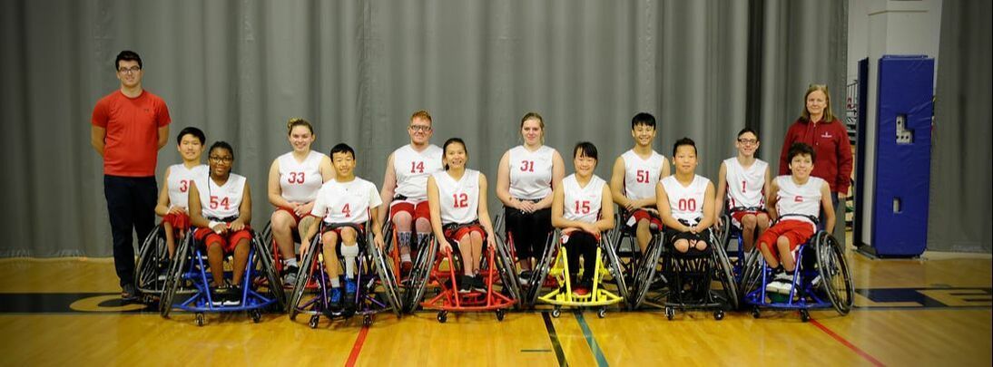 Team in white jerseys lines up in basketball chairs with two coaches