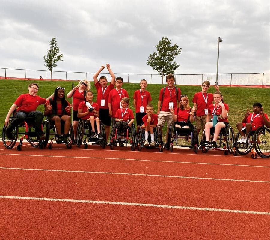 Track and field athletes in red shirts cheer on a track, many in wheelchairs
