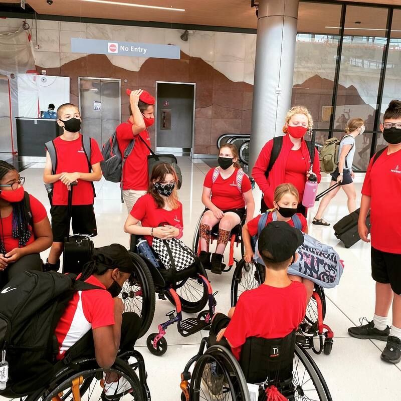 Masked athletes in red shirts gather with luggage in an airport terminal