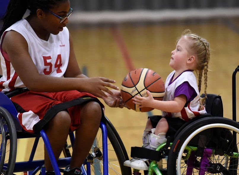 Player in jersey 54 hands a basketball to a young girl in a wheelchair