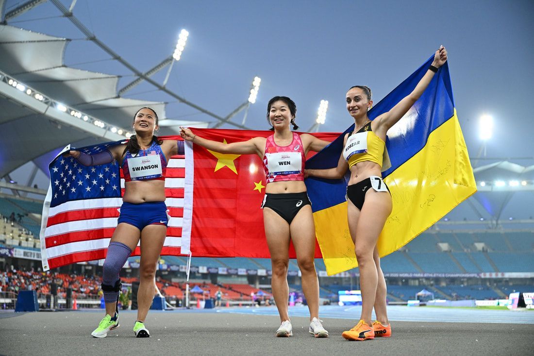 Three sprinters hold American, Chinese and Ukrainian flags on the track