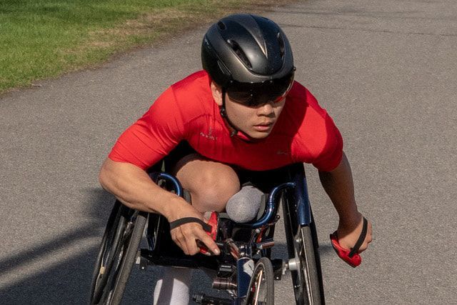 Racer in a red shirt and black visor helmet leans forward over a racing chair