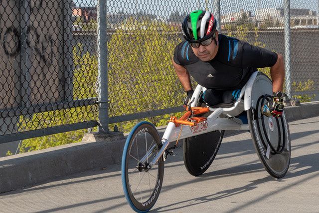 Racer in a green, white and red helmet crosses a fenced bridge