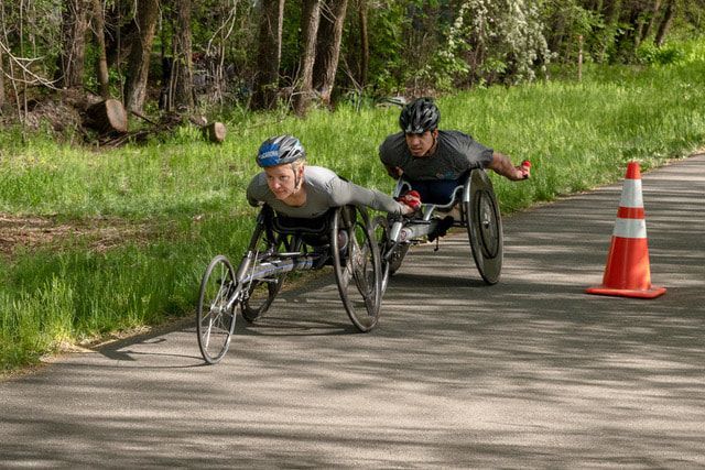 Two racers in gray shirts lean low in racing chairs beside an orange cone