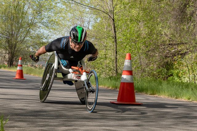 Racer in a green and black helmet leans into a turn past an orange cone