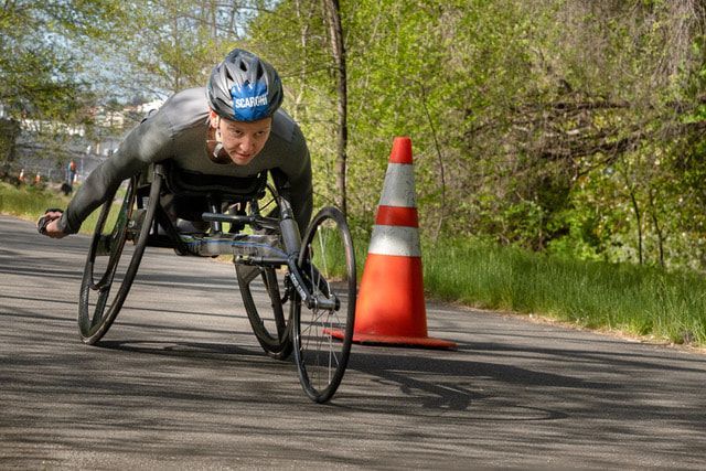 Racer in a gray shirt and blue helmet passes close to an orange cone